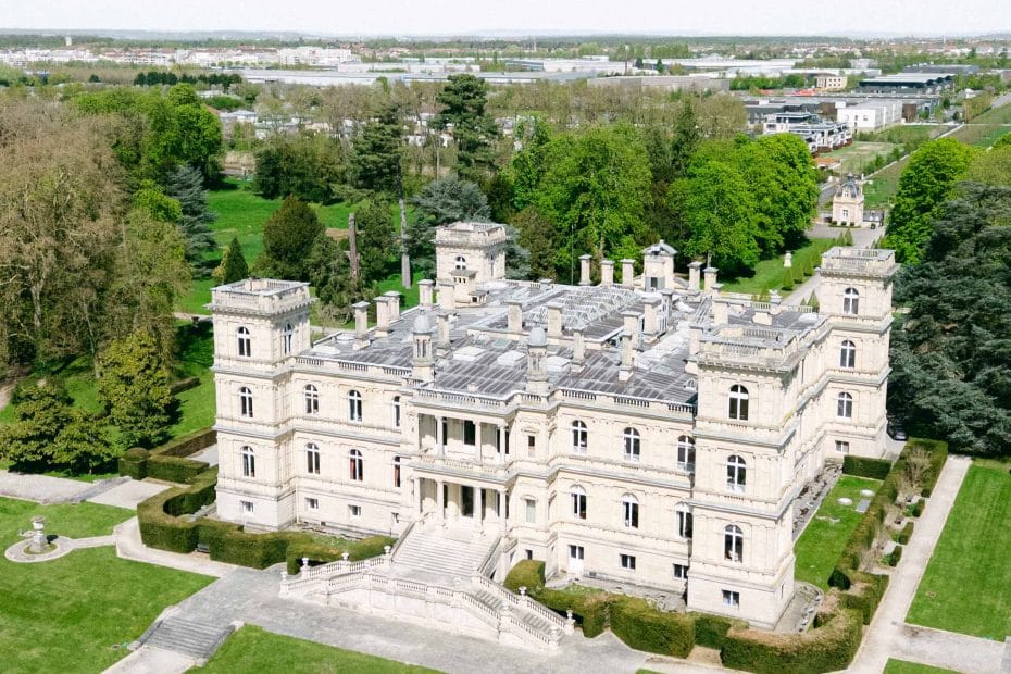 A large stone castle-like mansion with symmetrical towers and manicured gardens, viewed from above.