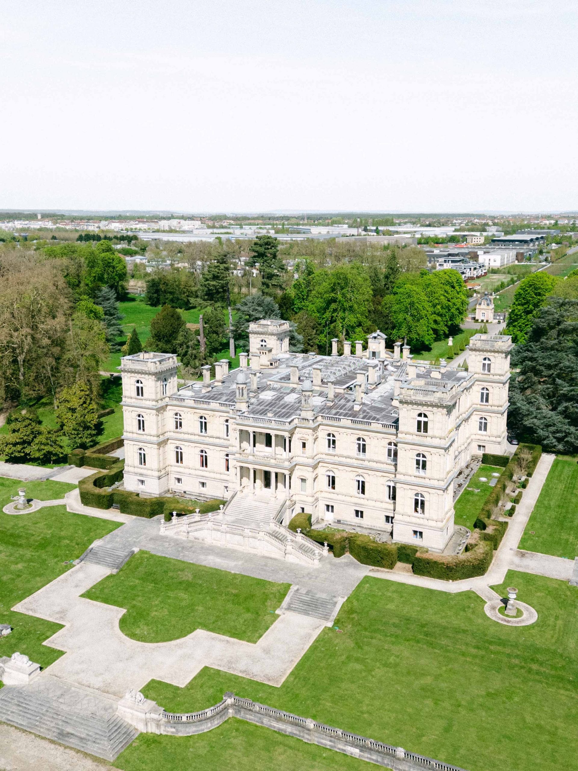 A large stone castle-like mansion with symmetrical towers and manicured gardens, viewed from above.